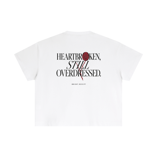 Back of the white Night Receipt boxy cotton tee with HEARTBROKEN, STILL OVERDRESSED in editorial serif capitals and a pressed oxblood rose blooming through the letterform