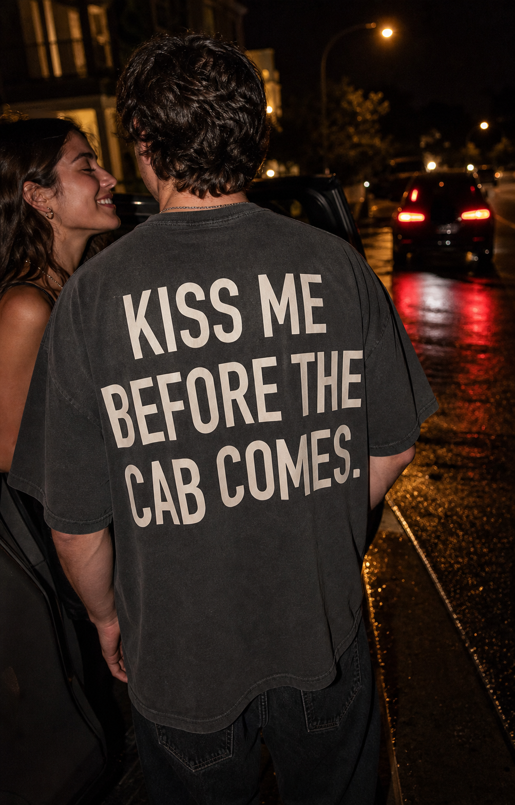 Couple on a night street, one wearing the black Night Receipt oversized tee with the cream KISS ME BEFORE THE CAB COMES back print
